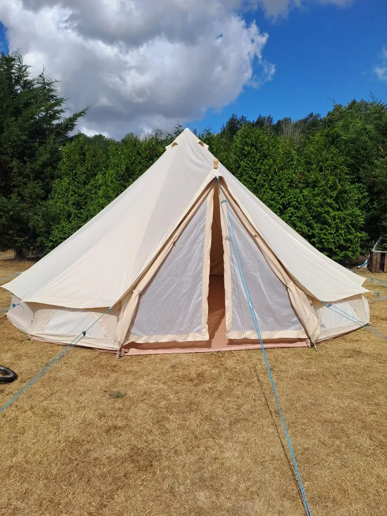 A cream bell tent with the mesh door closed in the grounds at Woodhill Campsite, Faversham, Kent