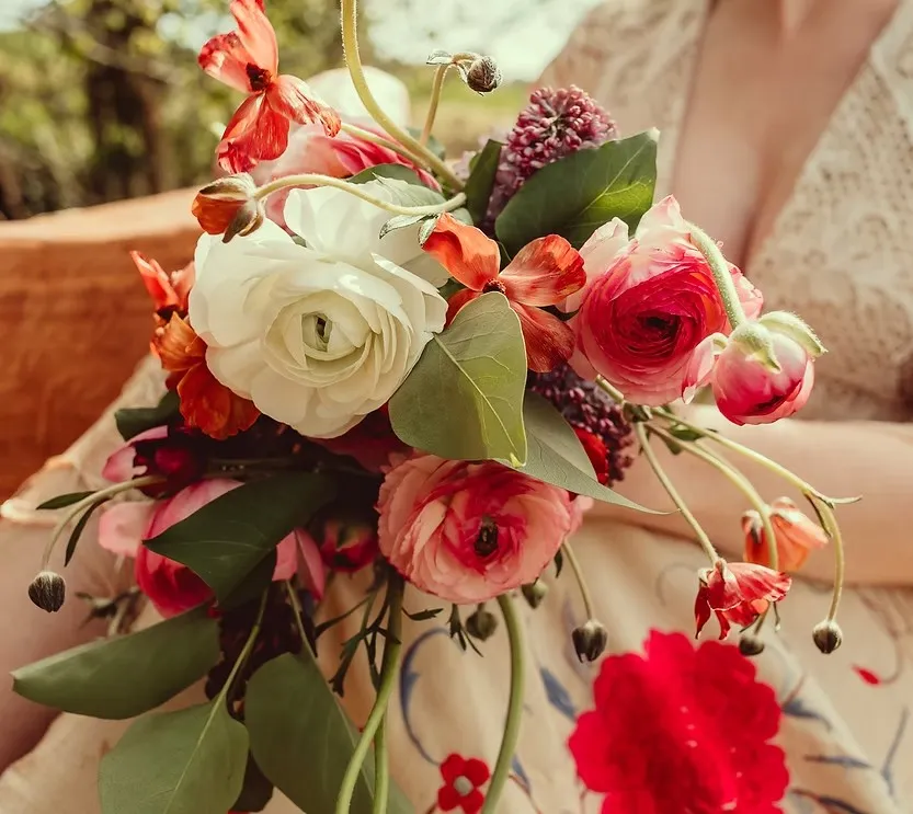 A colourful bridal bouquet of ranunculus, poppies and foliage held outdoors at Woodhill Weddings, Faversham, Kent