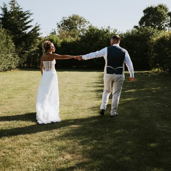 A bride and groom walking hand in hand across the lawn